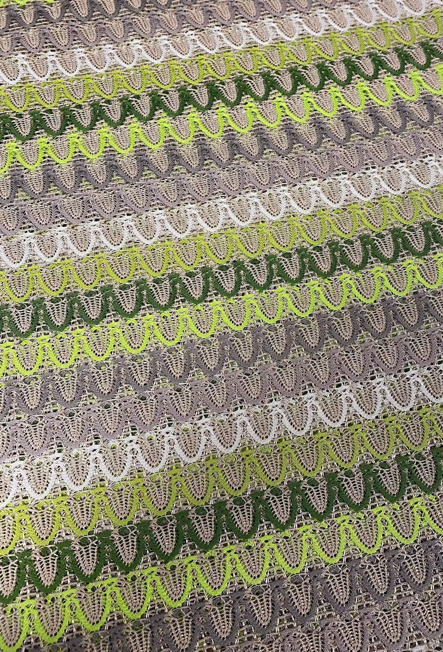 Close-up of beige and green zigzag knit jersey mesh fabric with lightweight, breathable texture for sewing and crafts