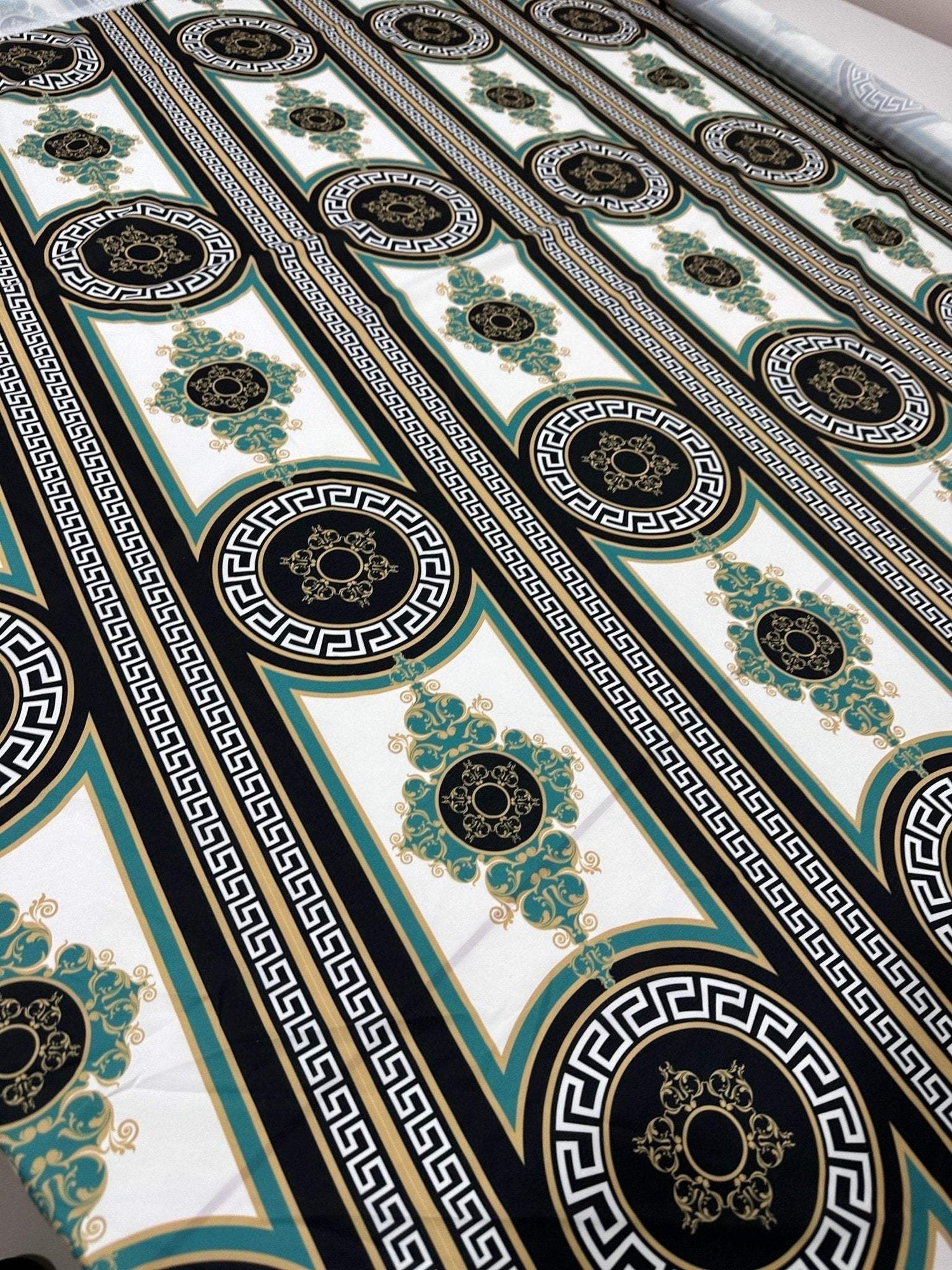 Greek Key Pattern Fabric with black, white, and gold intricate geometric and floral designs on a wide fabric roll