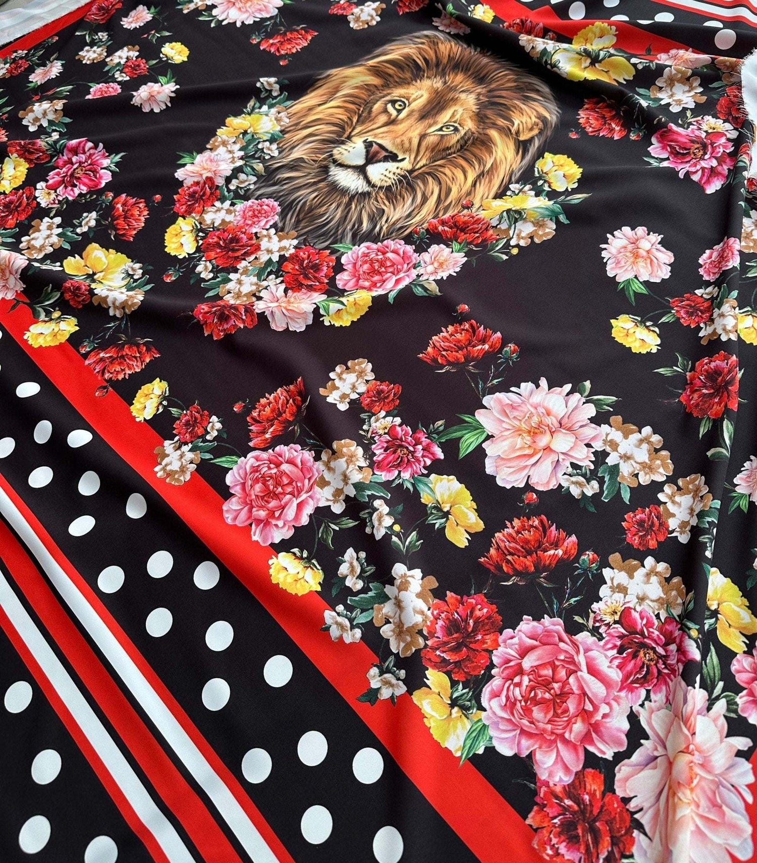Floral print fabric with vibrant flowers and a detailed lion face on black background, accented with red stripes and white polka dots.
