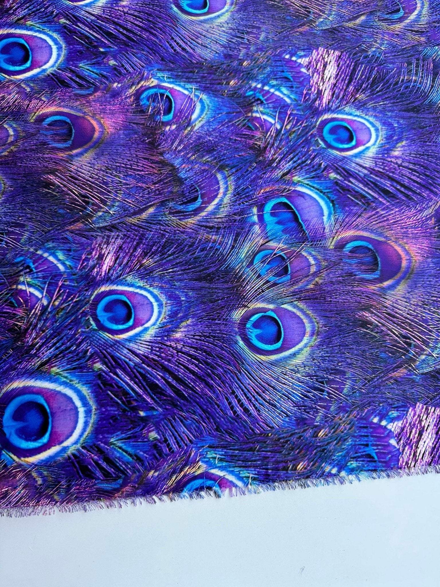 Close-up of purple fabric with vibrant peacock feather pattern and blue eye spots