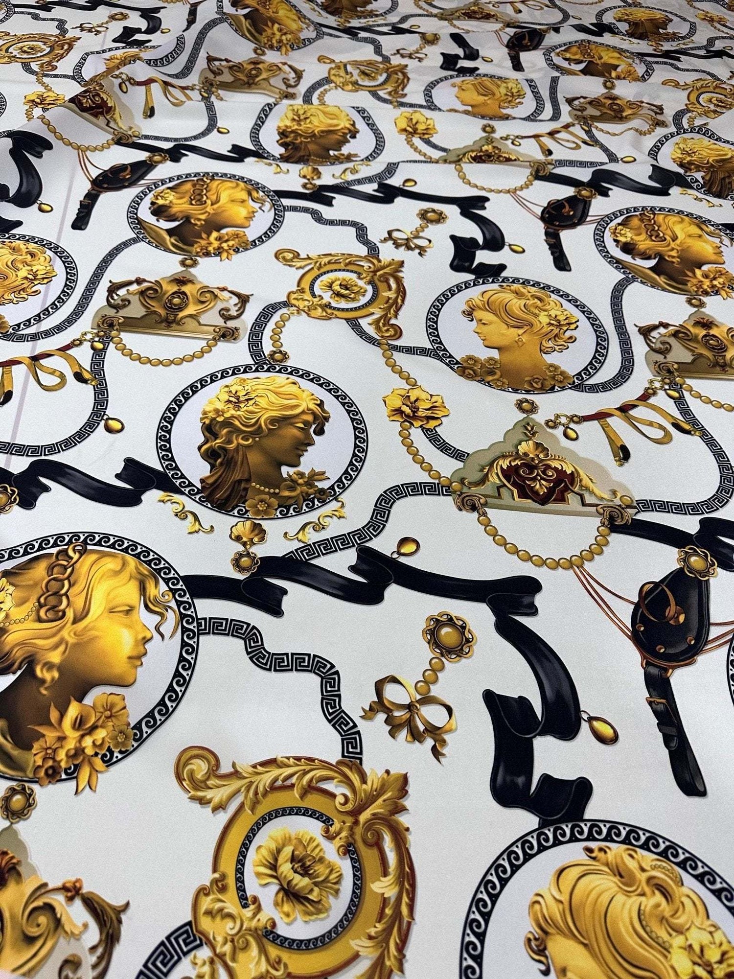 Queen and Rome Pattern crepe fabric with intricate gold and black classical portrait motifs on white background