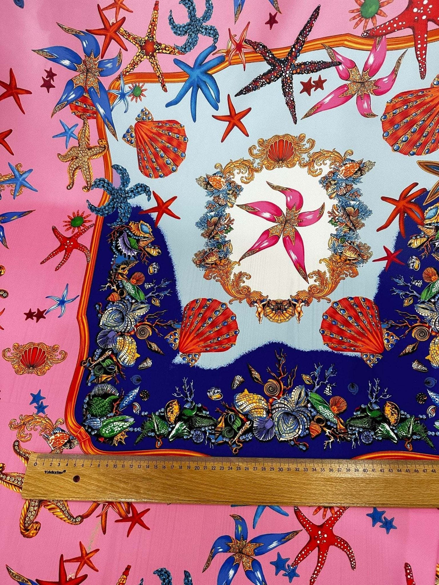 Coastal sea shell fabric with colorful starfish, shells, and marine patterns on a pink background with a measuring ruler