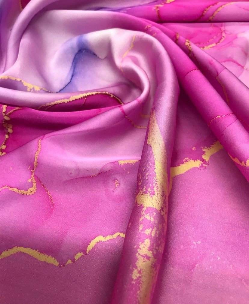 Close-up of vibrant tie dye fabric in pink and purple hues with gold accents and flowing texture