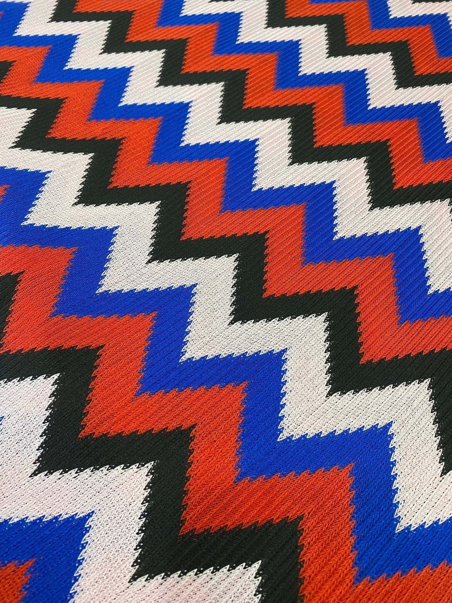 Luxury zigzag knit jersey fabric with vibrant blue, red, black, and sugar pink zigzag pattern, soft drape, and stretch for stylish garments