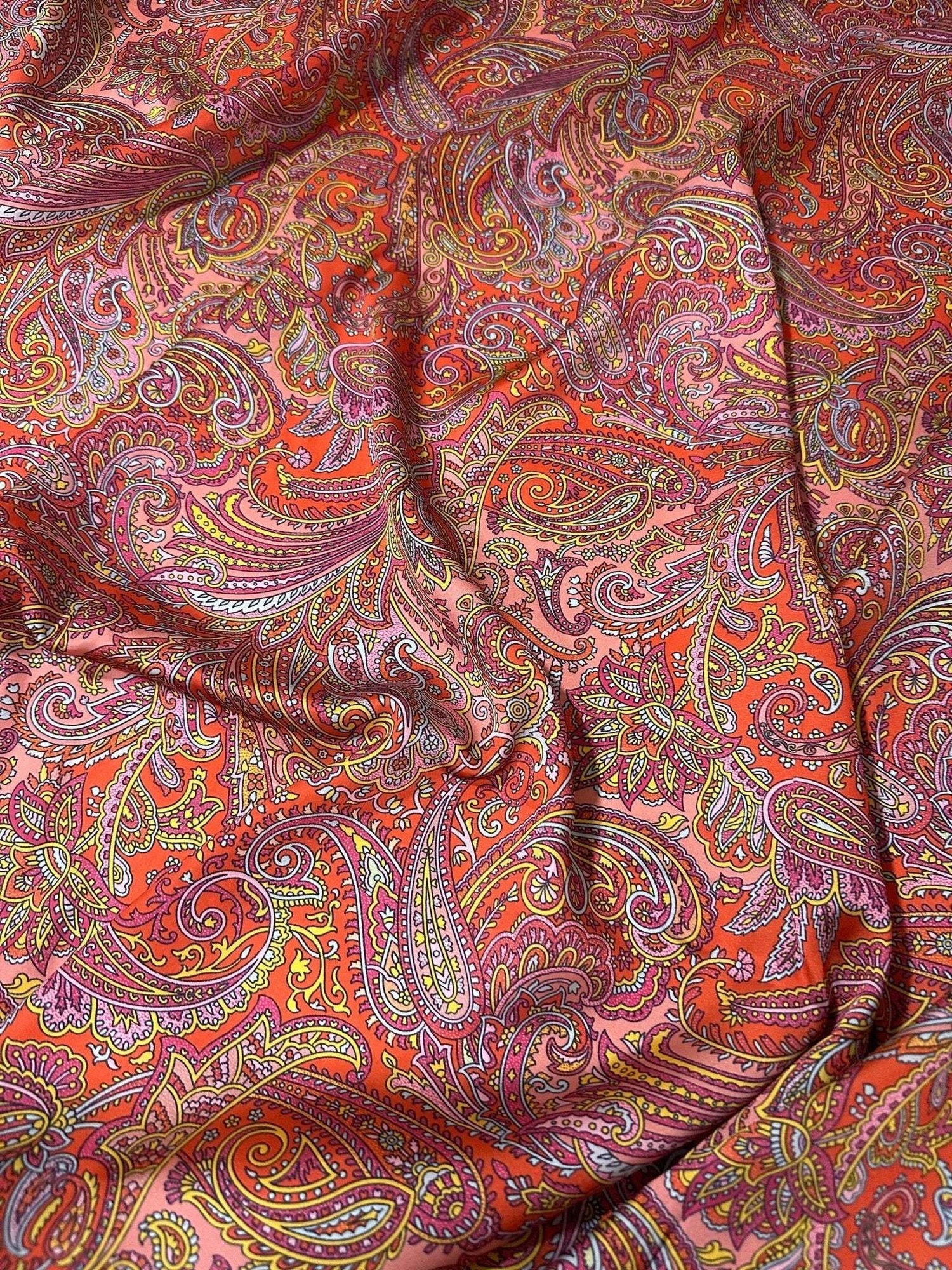 Colorful paisley pattern fabric with intricate designs in red, orange, and purple hues, ideal for sewing and crafting projects.